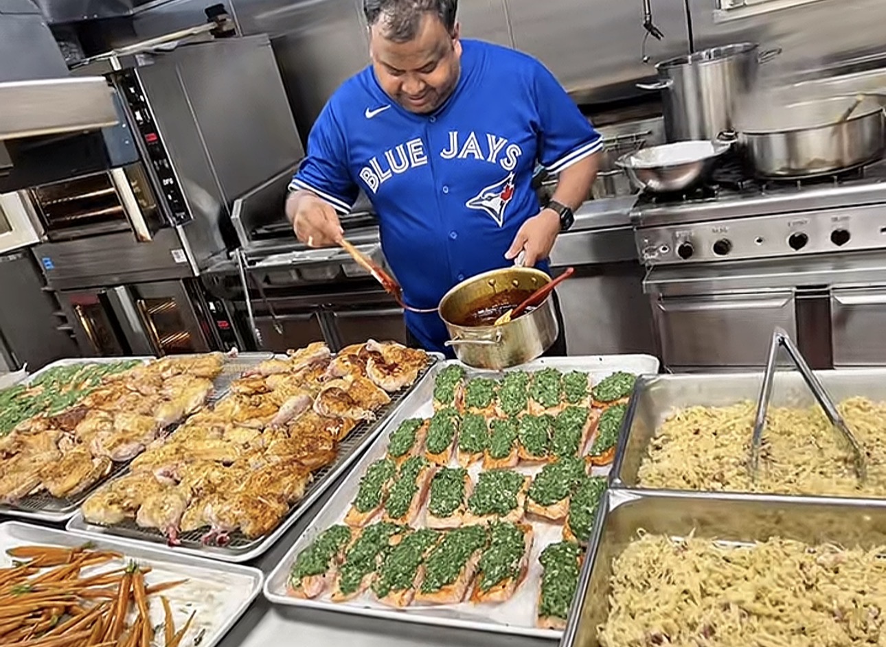 Chef Saku plating a large catering spread of chicken and salmon